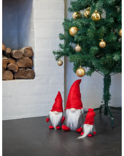 Set med tre julenissefigurer med långa vita skägg, röda mössor och grå kroppar, placerade under en julgran med guldkulor. Perfekt för juldekoration.