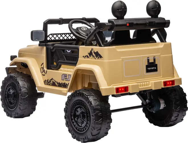 Beige elbil til børn, designet som en Toyota FJ Cruiser med store terrændæk, baglygter, bjergdekaler, to sæder, rat og sidespejle. Robust offroad-look.