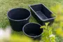 Sæt med tre sorte plastbeholdere: to runde og én rektangulær, alle med solide kanter. Velegnet til havearbejde, opbevaring eller praktisk brug. Vist udendørs på græs.