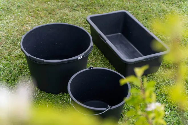 Sæt med tre sorte plastbeholdere: to runde og én rektangulær, alle med solide kanter. Velegnet til havearbejde, opbevaring eller praktisk brug. Vist udendørs på græs.