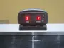 Digitalt airhockey-scoreboard med rød LED-skærm, viser hjem- og gæstescorer. Har tænd/sluk-knap, reset-knap og monteres på bordet. Kompakt sort plastdesign.