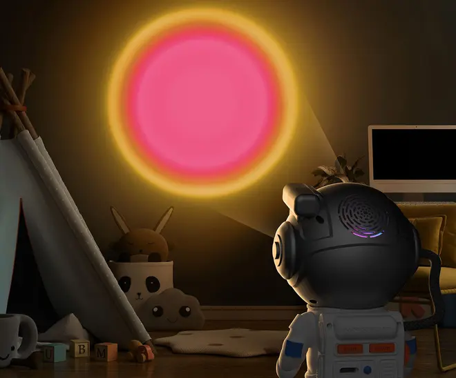 Børnenes natlampeprojektor formet som en astronaut, projicerer en glødende pink og gul sol på væggen. Velegnet til børneværelser, med plysdyr og legetelt synlige.
