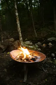Rund bålskål i metal med solide ben, brændende træ og kviste. Velegnet til udendørs brug, ideel til have eller camping. Rustbestandig og nem at rengøre.