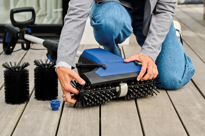 Elektrisk terrassebørste med udskiftelige sorte børstehoveder, blå og sort krop, ergonomisk håndtag. Perfekt til rengøring af træoverflader. Ekstra børstehoveder vises, person samler den.