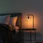 Moderne natbordslampe med sort metalstel og klar glaskuppel, placeret på et firkantet sidebord. Udsender varmt lys, ideel til soveværelser eller stuer.