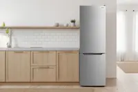 Høj, sølvfarvet køleskab med fryser nederst, grebsfrit design, placeret i et moderne køkken med lyse træskabe og hvid flisebagvæg. Stilrent og energieffektivt look.