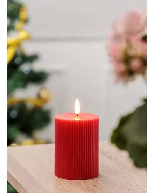 Rød søjlelys med lodret rillet struktur, brænder med en rolig flamme. Cylindrisk form, placeret på en træoverflade. Perfekt til boligindretning eller festlige lejligheder.