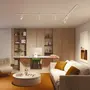 Moderne hjemmekontor med hvidt skrivebord, grøn stol, beige sofa med brune puder, rundt sofabord, indbyggede træhylder og loftsskinnebelysning. Varme, neutrale farver.