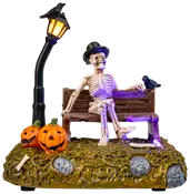 Halloweenprydnad med skelett i hög hatt på bänk, två urgröpta pumpor, gatlykta och en kråka. Basen är gräsig med stenar och ben.