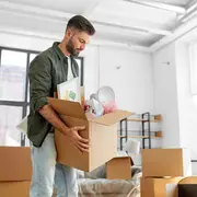 Brun flyttkartong med hushållsartiklar som inramad bild, lampa och inslagna föremål. Stabil konstruktion, lämplig för packning och transport vid flytt.