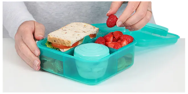 Turkis madkasse i plastik med fire rum, indeholder sandwich, jordbær, lille rund beholder og en snack. Sikker låg, perfekt til organiseret opbevaring og transport af mad.