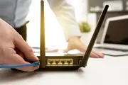 Trådløs router med to antenner, fire gule Ethernet-porte og én WAN-port. En hånd tilslutter et blåt Ethernet-kabel. Velegnet til internetforbindelse i hjemmet eller på kontoret.
