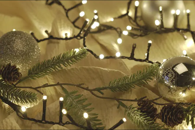 Varmhvide julelyskæder med sort ledning, fyrregrene, kogler og sølvkugler til festlig juledekoration.