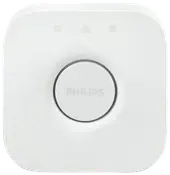 Hvid Philips Hue Bridge smart home-hub, firkantet med afrundede hjørner, central rund knap, diskret logo og tre små indikatorikoner øverst.