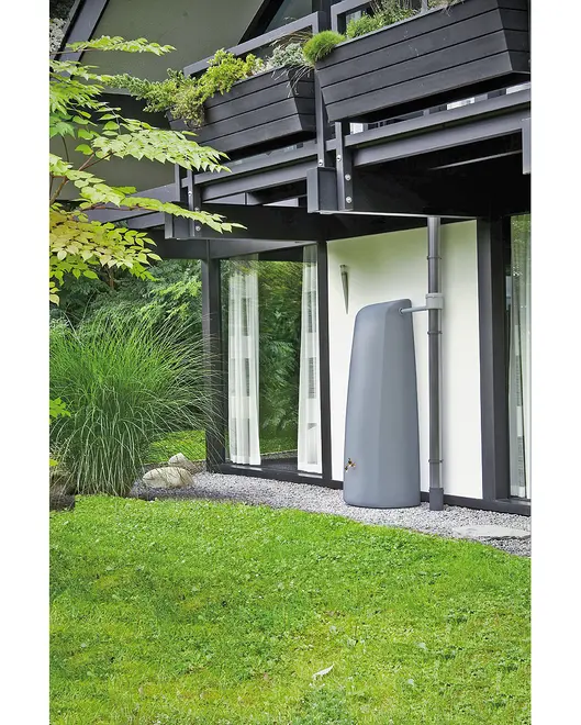 Høj, slank, grå regnvandstank med messinghane, tilsluttet nedløbsrør, placeret ved moderne husfacade til opsamling af regnvand til haven.