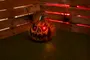 Halloweenpumpa med lysande röda LED-ögon, snidat skrämmande ansikte, texturerad orange yta och svart stjälk. Visas på konstgräs med träbakgrund.