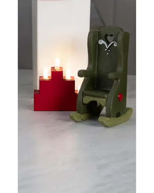 Miniatyr grøn trægyngestol med hjerteformet udskæring og hvide detaljer, vist ved siden af en rød trinformet lysestage med tændte lys.