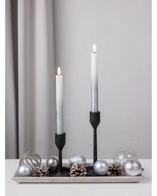 Dekorativt lysestagesæt med to sorte metalholdere, hvide stagelys, sølvkugler, kogler og glaskugler på et rektangulært fad. Elegant midterstykke til festlige lejligheder.
