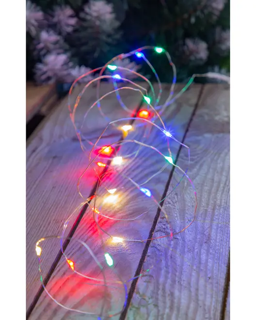 Thin, flexible wire with small LED lights spaced evenly along its length, emitting bright colors including red, green, blue, and yellow. The wire is arranged in loose coils on a wooden surface, and the lights create a festive, multicolored glow. The LEDs are compact and the wire is nearly invisible, making the lights appear to float.