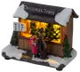 Miniatyr julgransstånd med snötäckt tak, belyst interiör, prisskylt och två figurer som handlar. Detaljerad, handmålad, perfekt för julby eller dekoration.