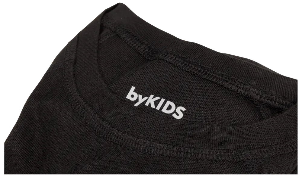 Närbild på svart barn-T-shirt med synliga sömmar och vitt "byKIDS"-tryck i nacken. Mjukt bomullstyg, rund halsringning.