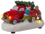 Dekorativ figur med röd lastbil, julgran och två personer som skjuter genom snö. Med lysande strålkastare, basljus, vinterkläder och snötäckt bas.