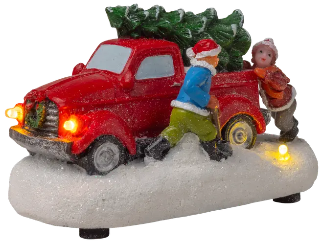 Dekorativ figur med röd lastbil, julgran och två personer som skjuter genom snö. Med lysande strålkastare, basljus, vinterkläder och snötäckt bas.