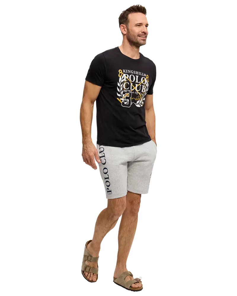 Herrset med svart t-shirt med texten “Kingshill Polo Club” och ljusgrå shorts med “Polo Club” på benet. Modellen bär bruna sandaler. Ansiktet är suddigt.