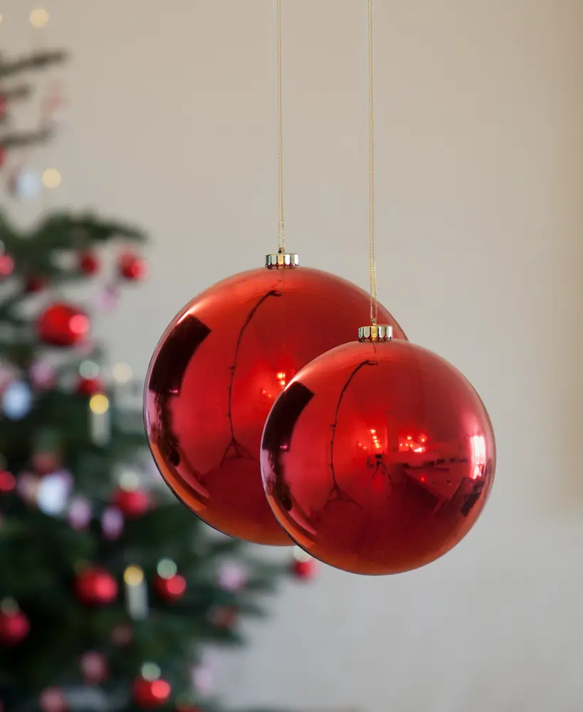 To store, skinnende røde julekugler med guldfarvede ophæng og snore. Perfekte til juletræspynt. Sløret juletræ med lignende kugler i baggrunden.