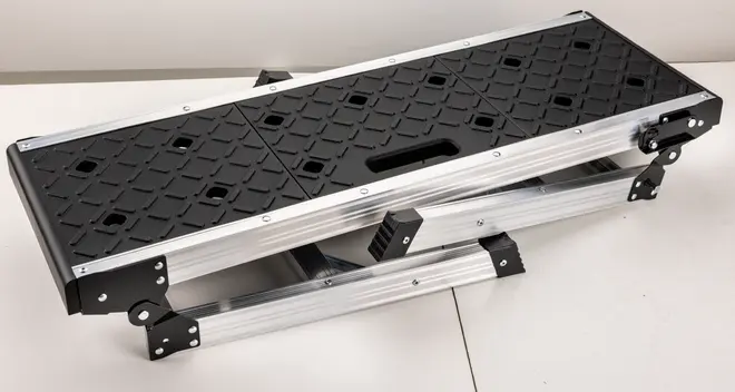 Sammenklappelig arbejdsplatform i aluminium med sort skridsikker overflade, diamantmønster og indbygget bærehåndtag. Robust og kompakt, nem at opbevare og transportere.