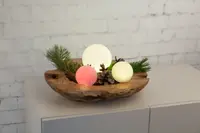 Dekorativt arrangemang med tre lysande glaskulor i vitt och rosa, konstgjorda grankvistar och kottar i en rustik träskål. Perfekt för festlig inredning.