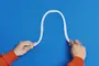 Fleksibel hvid plasttube, bøjet i S-form, holdt af to hænder. Perfekt til kabelstyring eller organisering af ledninger. Glat overflade, let og nem at forme.
