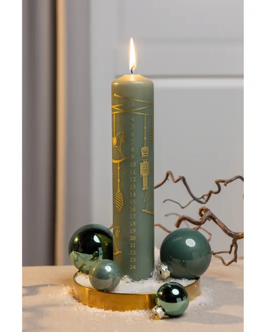 Grönt blockljus med guldfärgade adventssiffror och julmotiv, omgiven av gröna glaskulor på ett guldfat med konstsnö, perfekt för juldekoration.