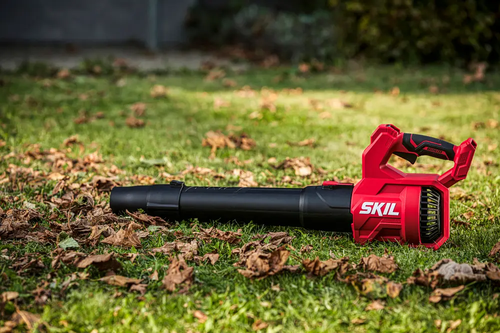 Röd och svart SKIL batteridriven lövblås med ergonomiskt handtag, lätt design och lång munstycke, perfekt för att rensa löv och skräp från gräsmattor och utomhusytor.