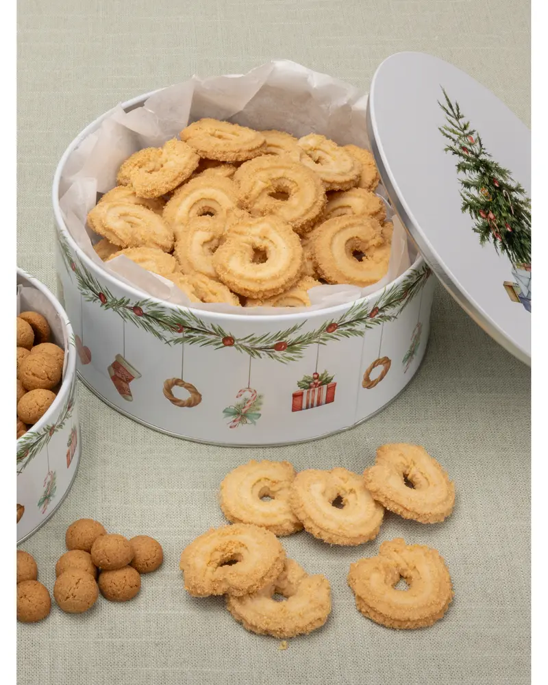 Runde smørkager i en festlig dåse dekoreret med julemotiver, herunder et juletræ og gaver. Kagerne er gyldne, sprøde og ligger på hvidt bagepapir i dåsen.