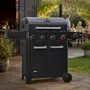 Sort gasgrill med fire kontrolknapper, to sidehylder, dobbeltlåge opbevaringsskab og indbygget termometer. Robust design med hjul, ideel til udendørs madlavning.