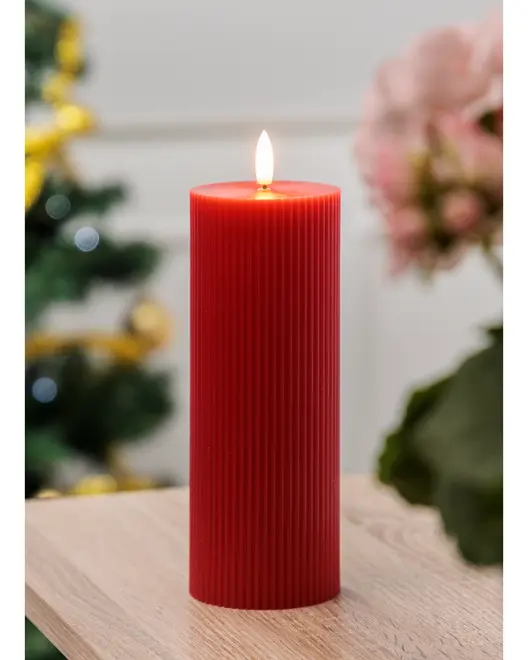 Høj rød søjlelys med lodret rillet struktur, brændende med en jævn flamme. Perfekt til dekoration eller festlig brug. Står på lyst træbord.