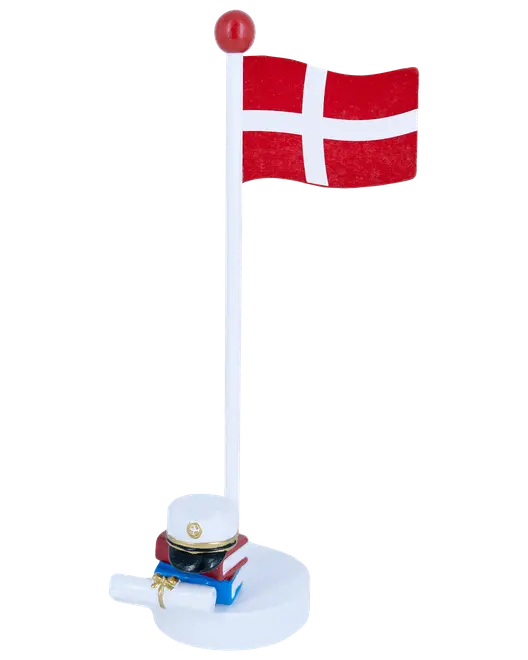 Dekorativt Dannebrog på hvid stang med rød top, pyntet med studenterhue, bøger og eksamensbevis ved foden. Perfekt til studenterfest eller som minde.
