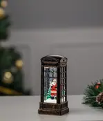 Dekorativ lykta formad som en gammaldags telefonkiosk med tomtefigur, gran och konstsnö inuti. Perfekt för juldekoration på bord eller spiselkrans.
