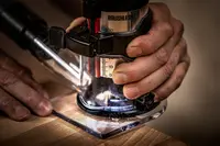 Kompakt borstlös träfräs med genomskinlig bas, ergonomiskt grepp och djupmätare, visas i bruk på träyta för exakt träbearbetning och kantfinish.