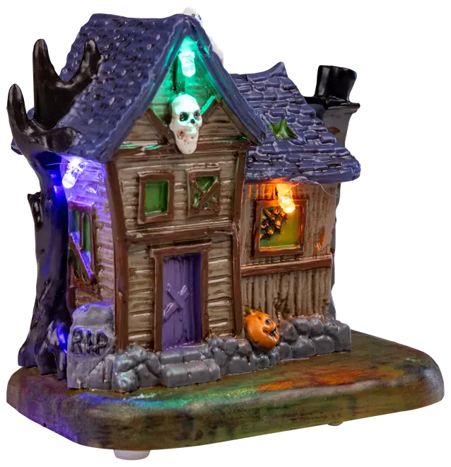 Miniatyrspökhus med lila tak, brädade fönster, dödskalle, pumpa och färgade LED-lampor. Inkluderar "RIP" gravsten, perfekt för Halloween-dekoration.