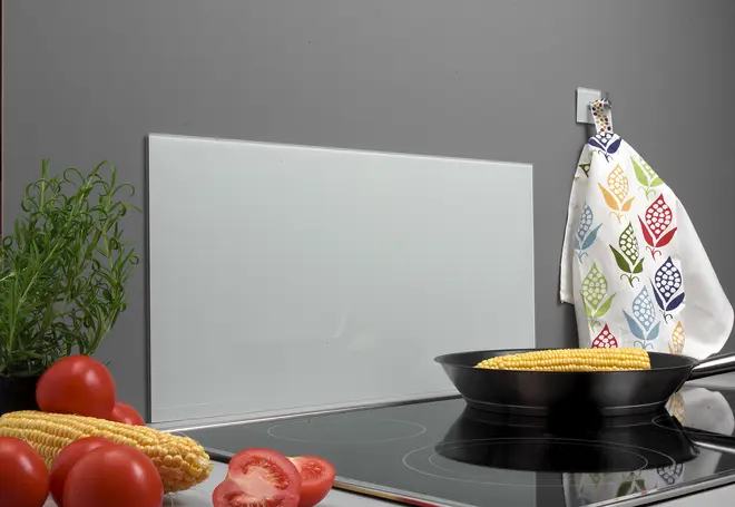 Vit, rektangulär glasskyddsplatta för kök, monterad bakom spishäll. Modern design, lätt att rengöra, skyddar väggen mot stänk. Visas med köksredskap och grönsaker.