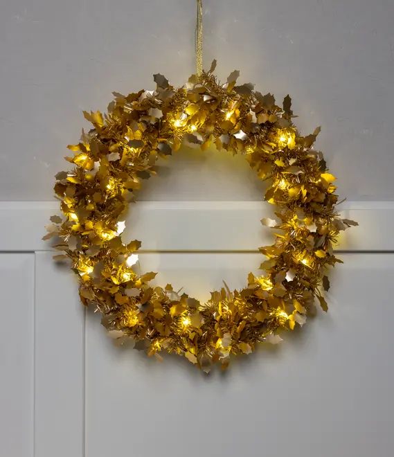 Guldmetal krans med blade formet som kristtorn, dekoreret med varme hvide LED-lys. Rundt design, velegnet til ophængning på døre eller vægge som julepynt.