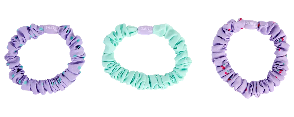 Sæt med tre elastikker: to lilla og én mintgrøn. Alle er lavet af glat, rynket stof, hvoraf den ene lilla har små farvede prikker som dekoration.