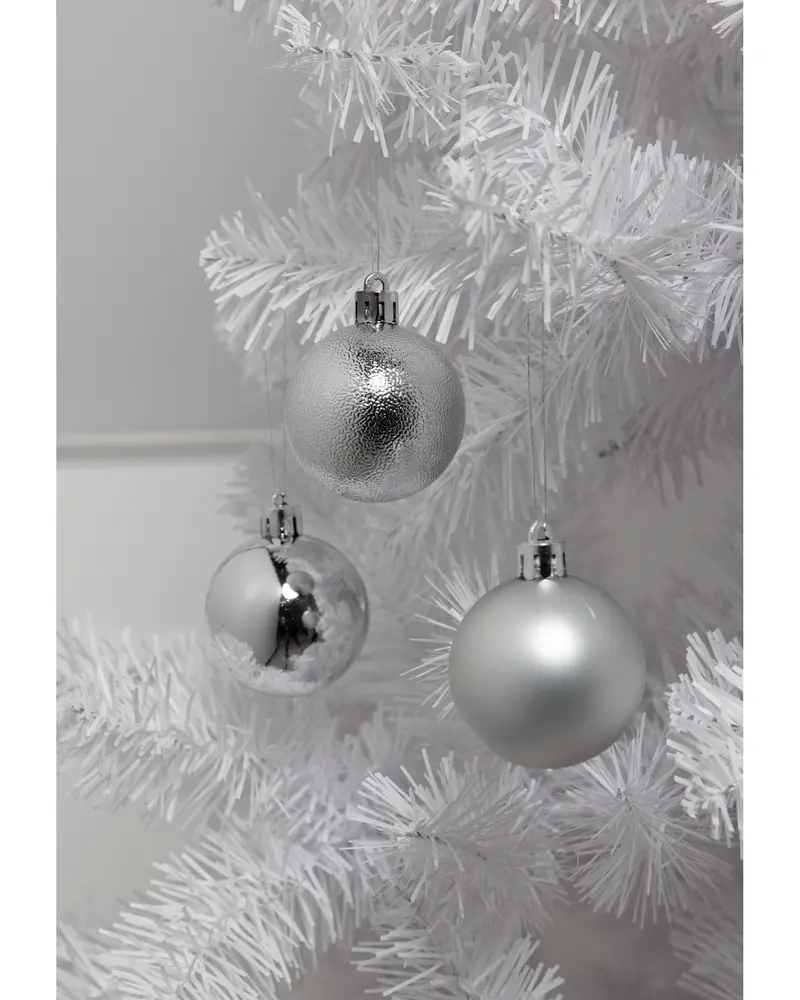 Set med tre silverfärgade julgranskulor med matt, blank och texturerad yta, hängande på en vit konstgjord gran. Varje kula har en metallkapsel för upphängning.