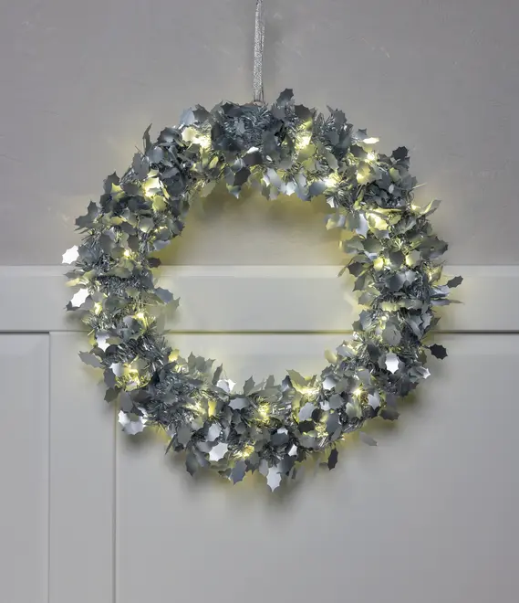 Sølvfarvet krans med kristtornformede blade og varme hvide LED-lyskæder. Rundt design, velegnet til ophæng som julepynt. Batteridrevet, kun til indendørs brug.