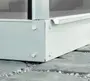 Närbild av växthusets metallhörn med synliga bultar, placerat på stenplattor. Konstruktionen har en robust, galvaniserad stålram och polykarbonatpaneler.