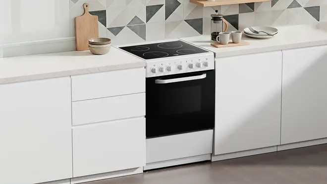 Fristående elektrisk ugn med svart glaslucka, vitt kontrollpanel och fyrzons keramikhäll. Passar mellan vita köksskåp. Modern och minimalistisk design för samtida kök.