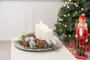 Dekorativt fat med två vita blockljus, silverkulor, kottar, bruna stenar och gröna kvistar, arrangerat som juldekoration. Julgran och nötknäppare i bakgrunden.