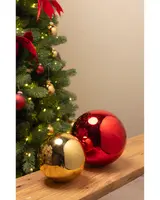Sæt med to store julepyntskugler, én blank rød og én blank guld, kugleformede, reflekterende overflade, velegnet til indendørs juledekoration, placeret på træoverflade nær juletræ.